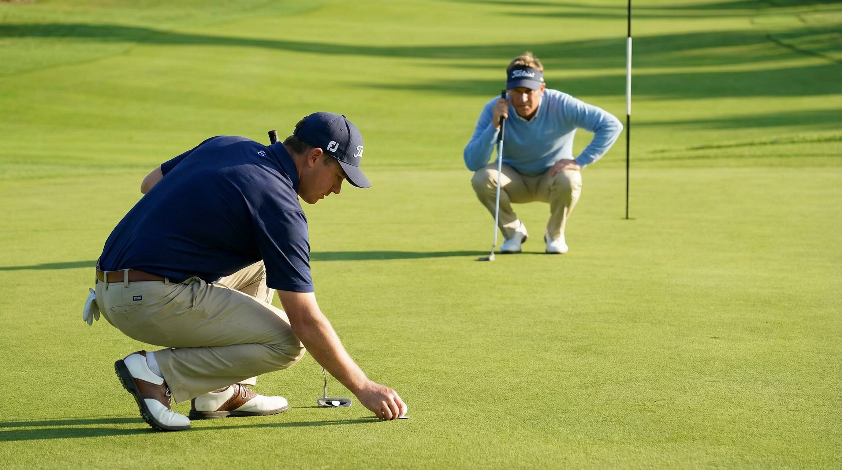 A golfer carefully marking their ball on the green with a ball marker while another golfer lines up their putt in the background.