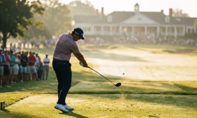 Golfer hitting driver from tee box on championship course, early morning golden hour lighting