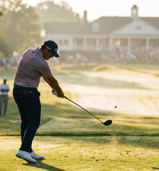 Golfer hitting driver from tee box on championship course, early morning golden hour lighting