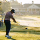 Golfer hitting driver from tee box on championship course, early morning golden hour lighting