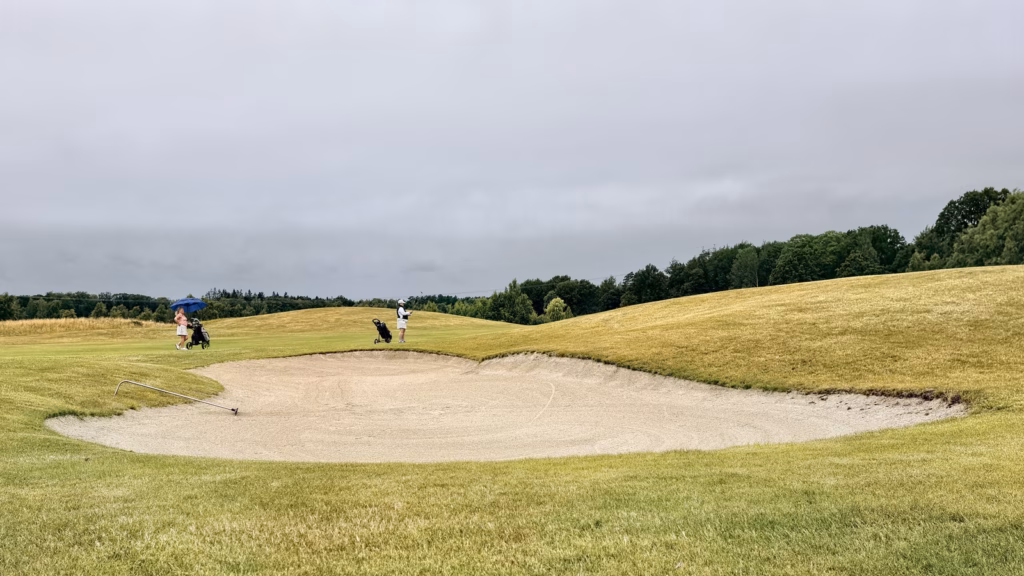 Two golfers and their bags beyond a bunker, illustrating a foursomes alternate shot partnership.