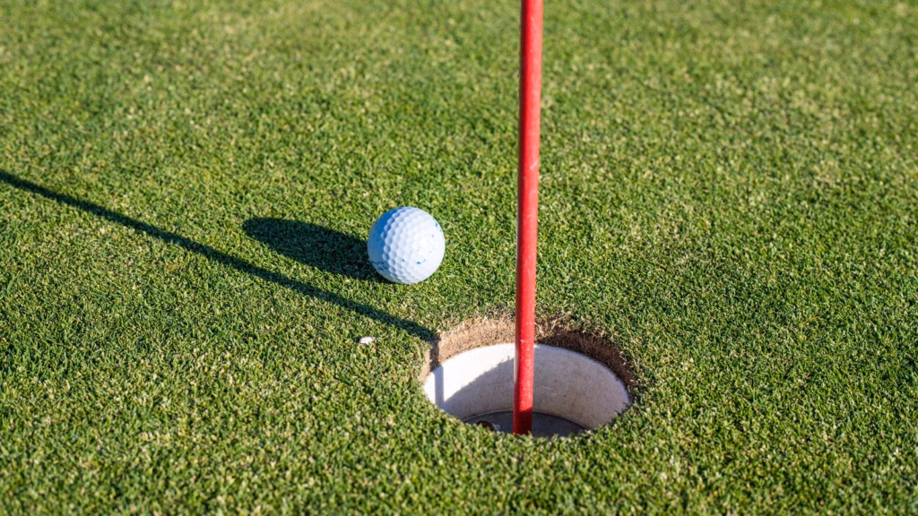 White golf ball beside the cup and flagstick, illustrating when to pick up in a golf scramble.